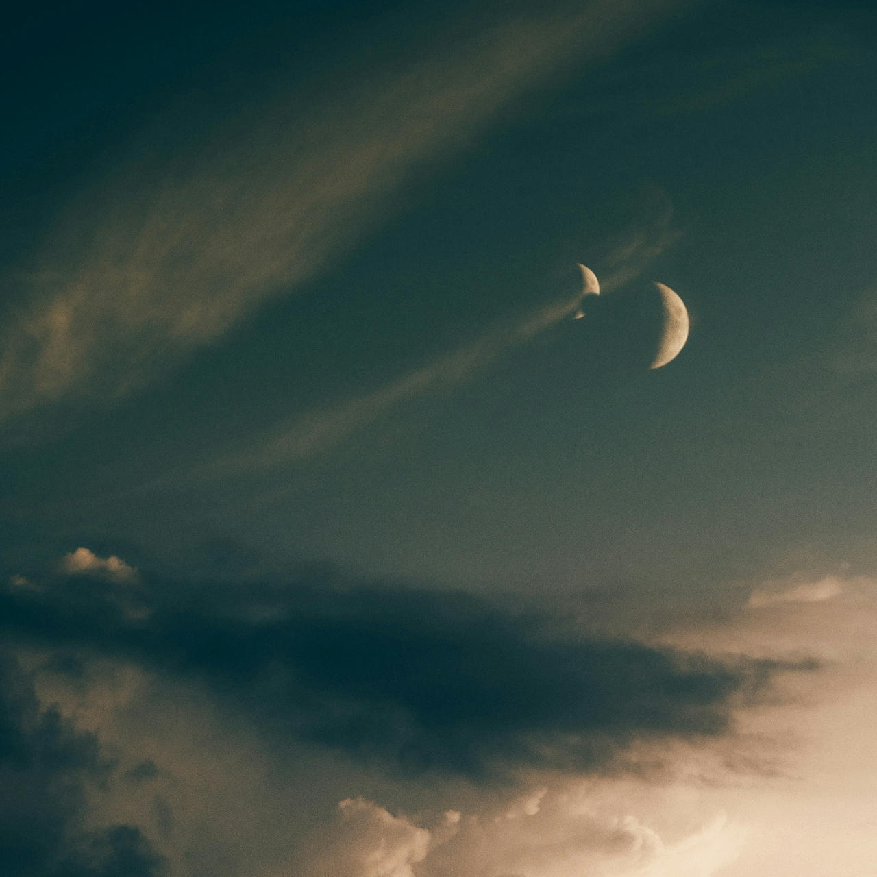 A blue-green sky with wispy clouds featuring two moons, one casting a shadow on the other